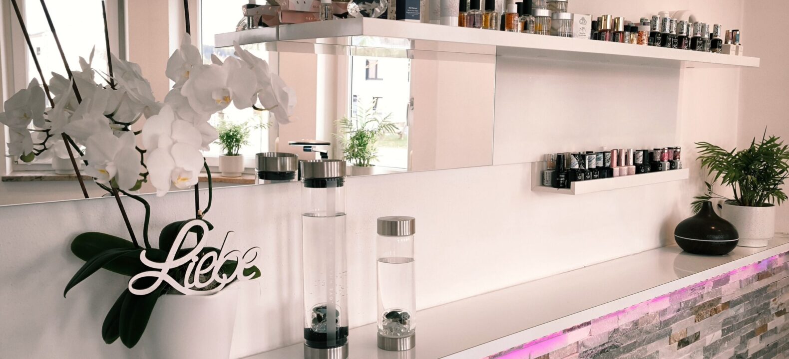 Innenansicht des Studios mit weißem Tresen, bequemer Behandlungsliege für Fußpflege und stilvoller Wandgestaltung in Rosa.