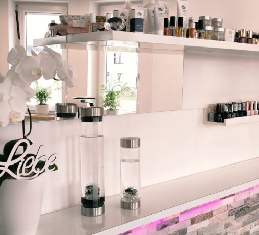 Innenansicht des Studios mit weißem Tresen, bequemer Behandlungsliege für Fußpflege und stilvoller Wandgestaltung in Rosa.