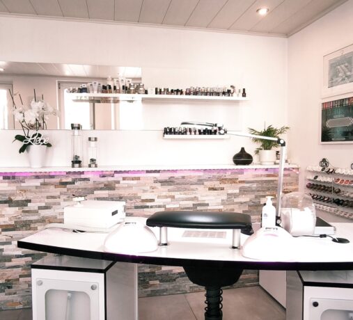Hell eingerichteter Arbeitsplatz im Nageltraum Nagelstudio mit Profi-Nageltisch, LED-Lampen, Farbauswahl und Zertifikaten an der Wand.